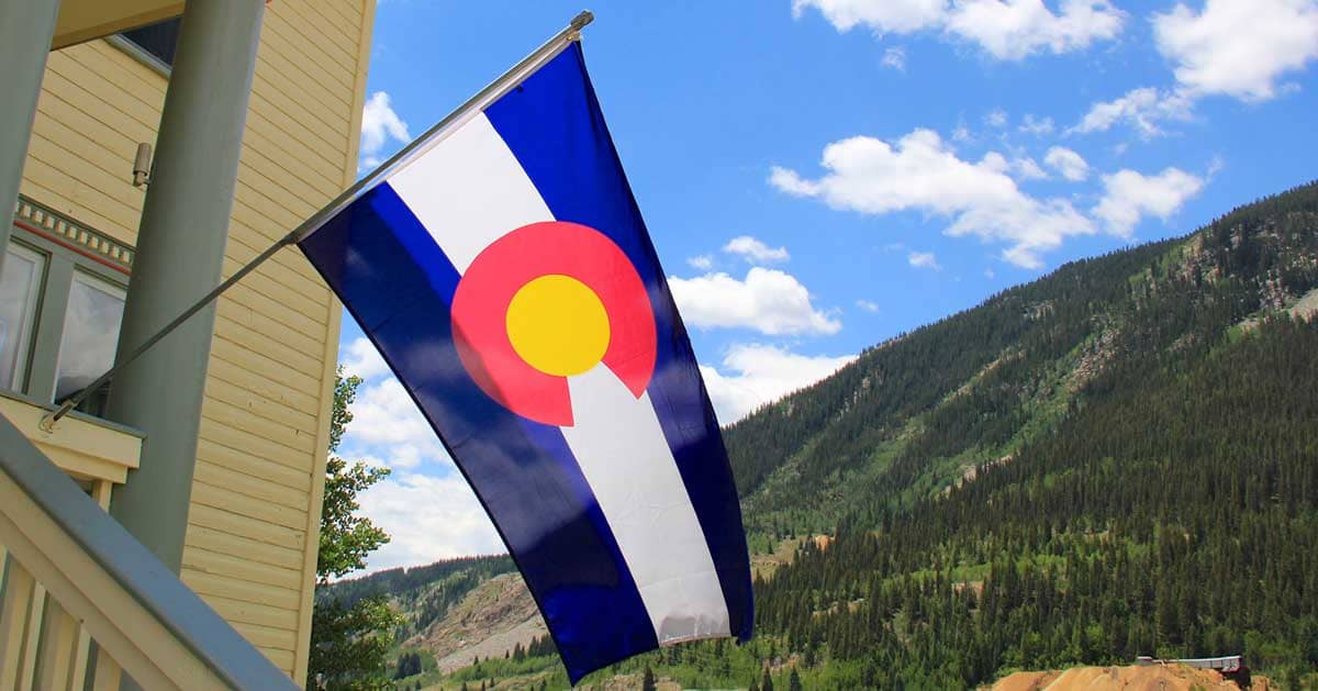 Colorado flag in front of a home with mountains and blue sky in the background