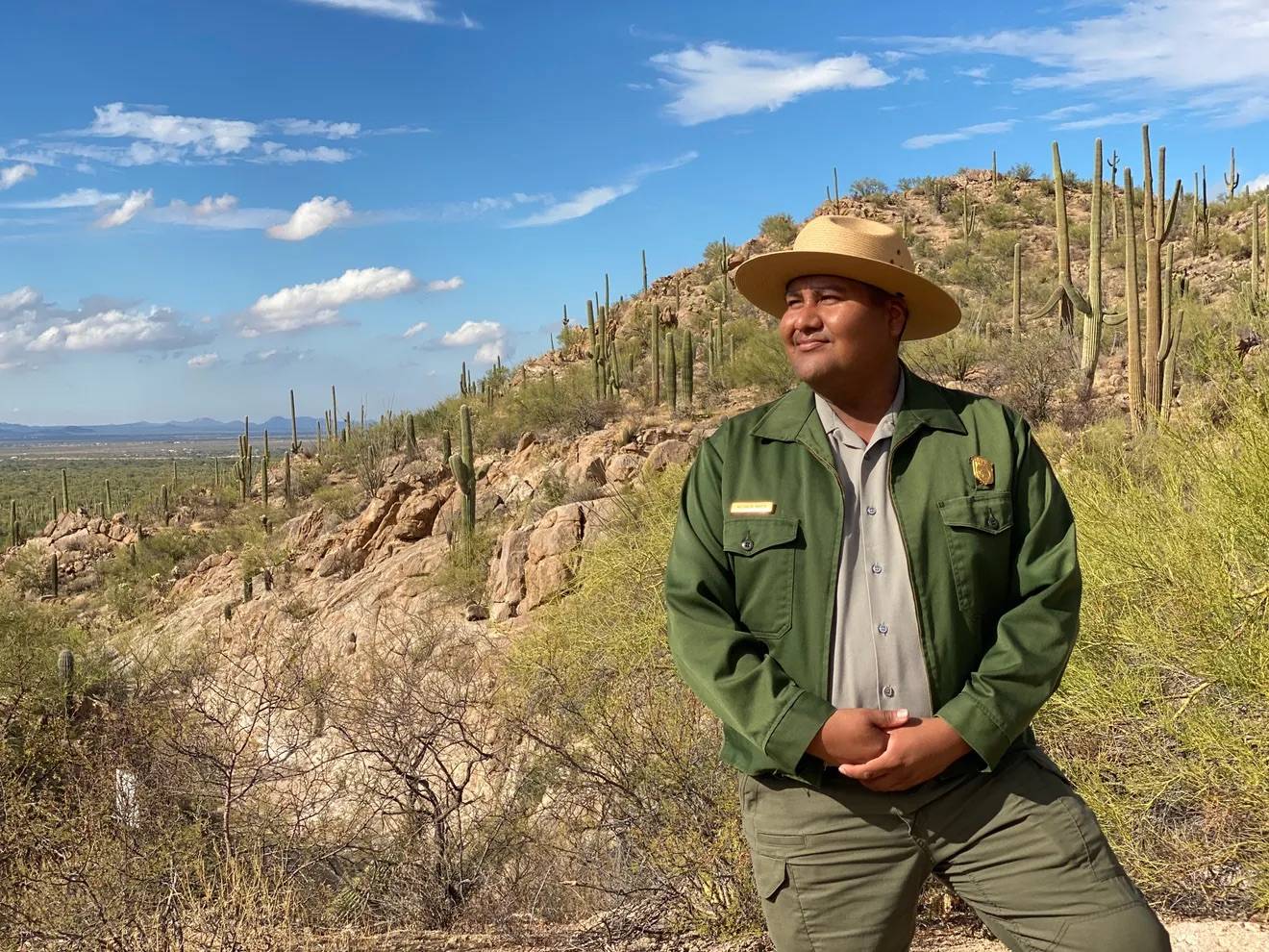 A uniformed national park worker standing in Saguaro national park looking off-camera