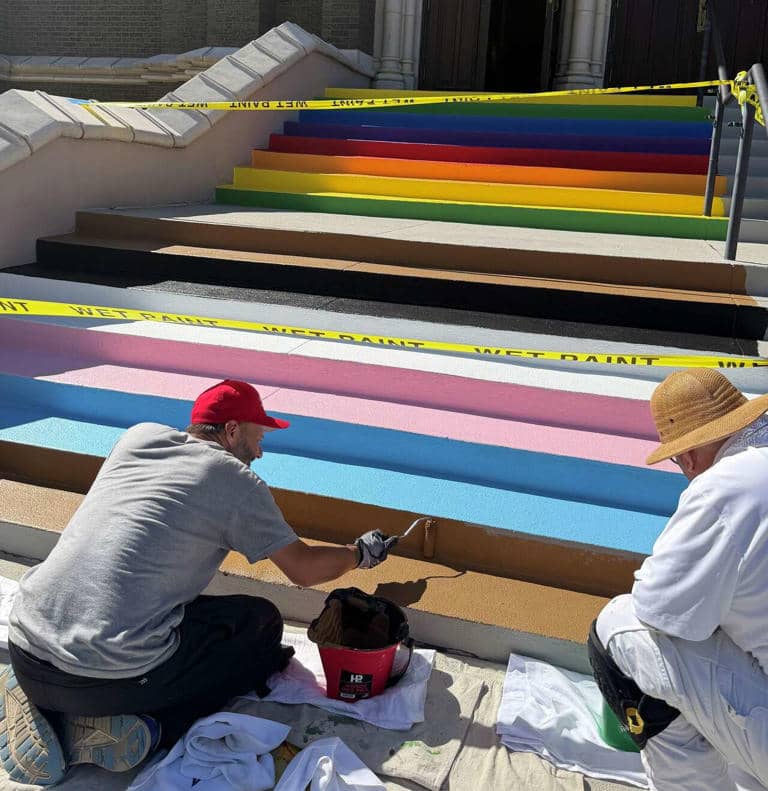 Two people painting steps, with finished rainbow-colored steps painted above them