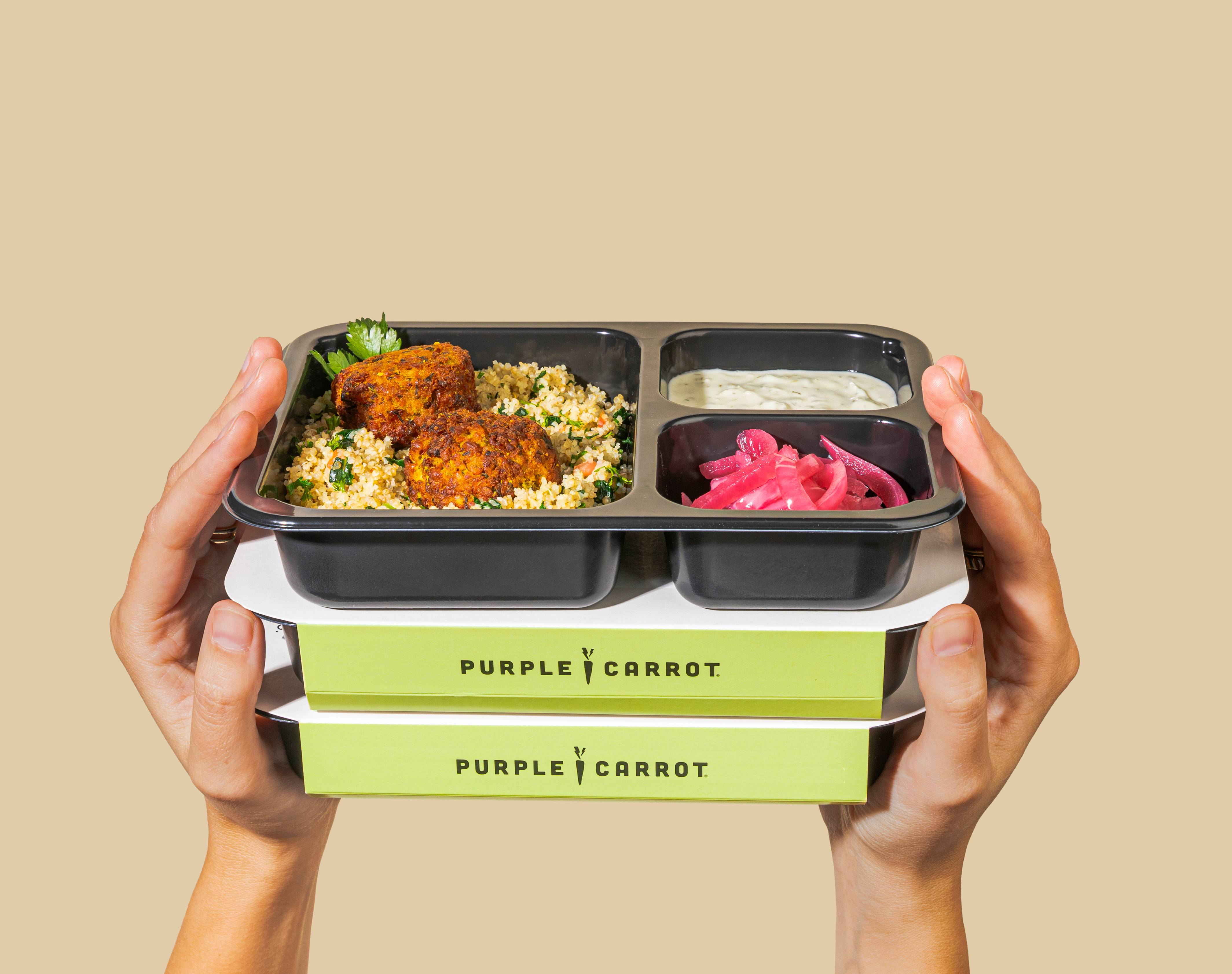 Three boxes of pre-made Purple Carrot meals held up by two hands