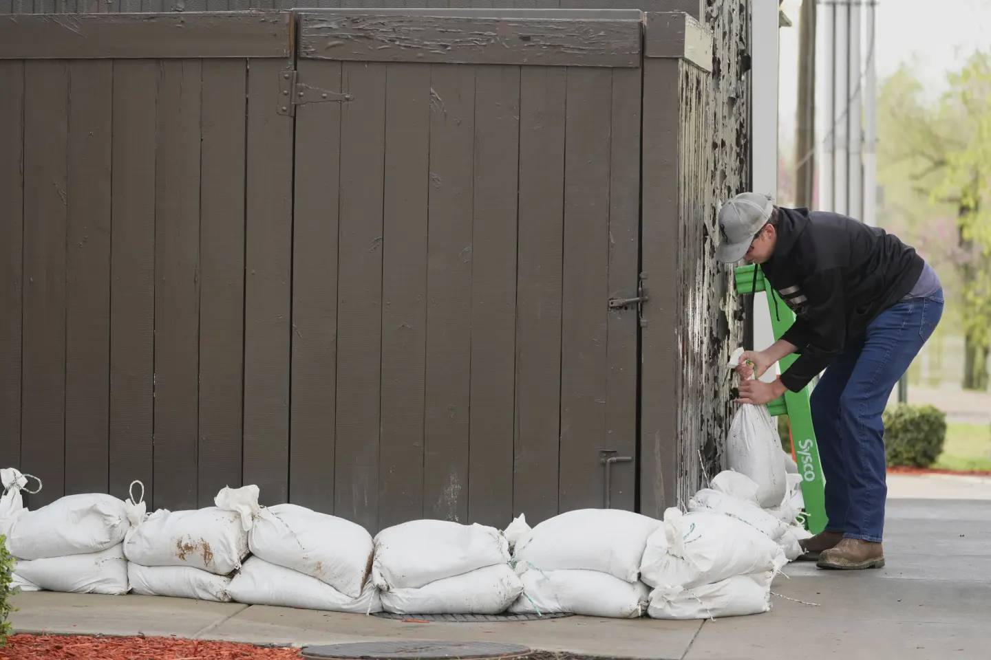 Person puts white sandbags in front of a brown exterior