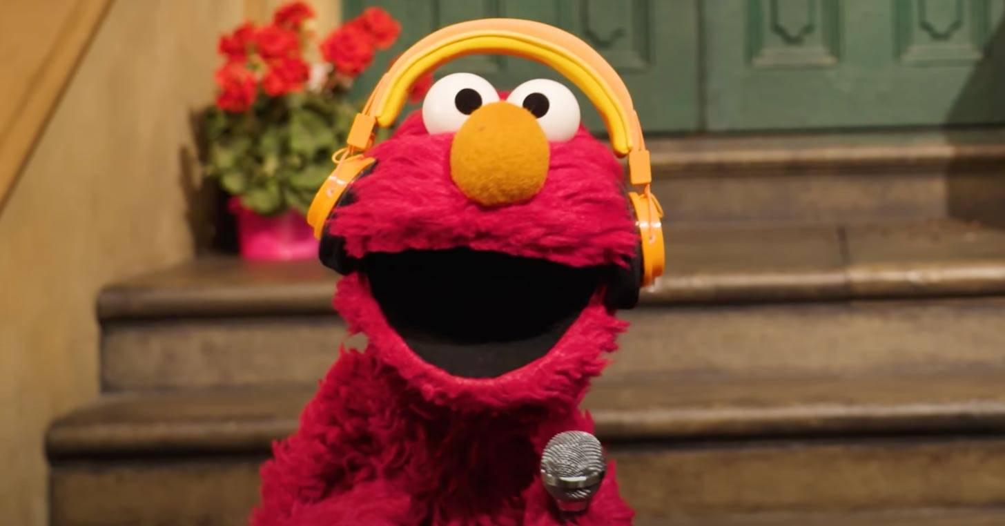 Elmo wearing yellow headphones holding a microphone