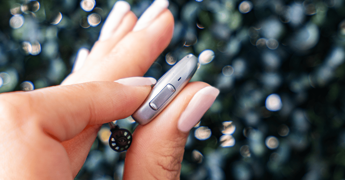 A close-up of a hand holding a silver hearing aid