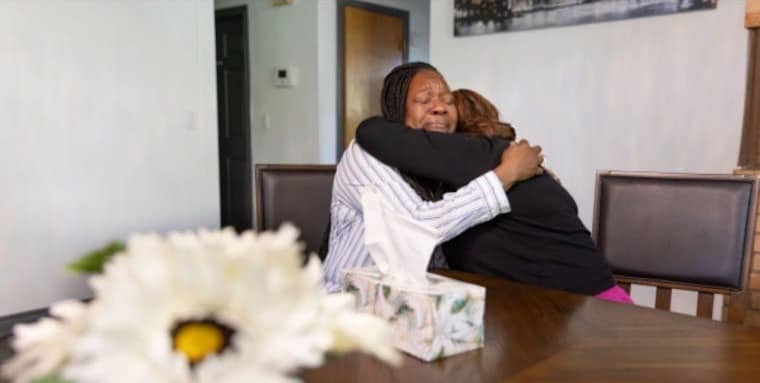 Two people hugging at a large table with blurry flowers in the foreground