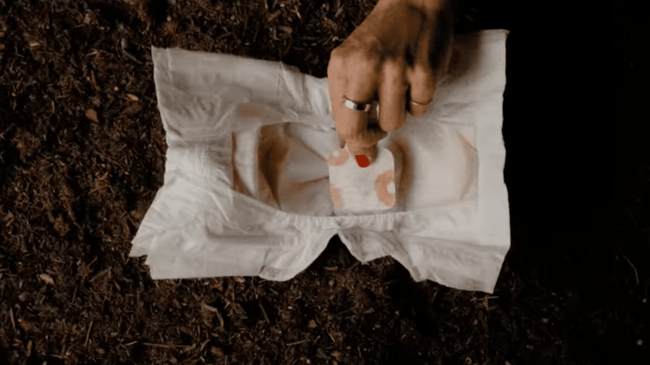 Hand putting something in a diaper surrounded by brown soil