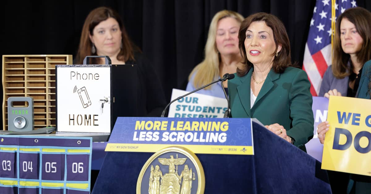 Kathy Hochul speaking at a podium that says "More learning, less scrolling"