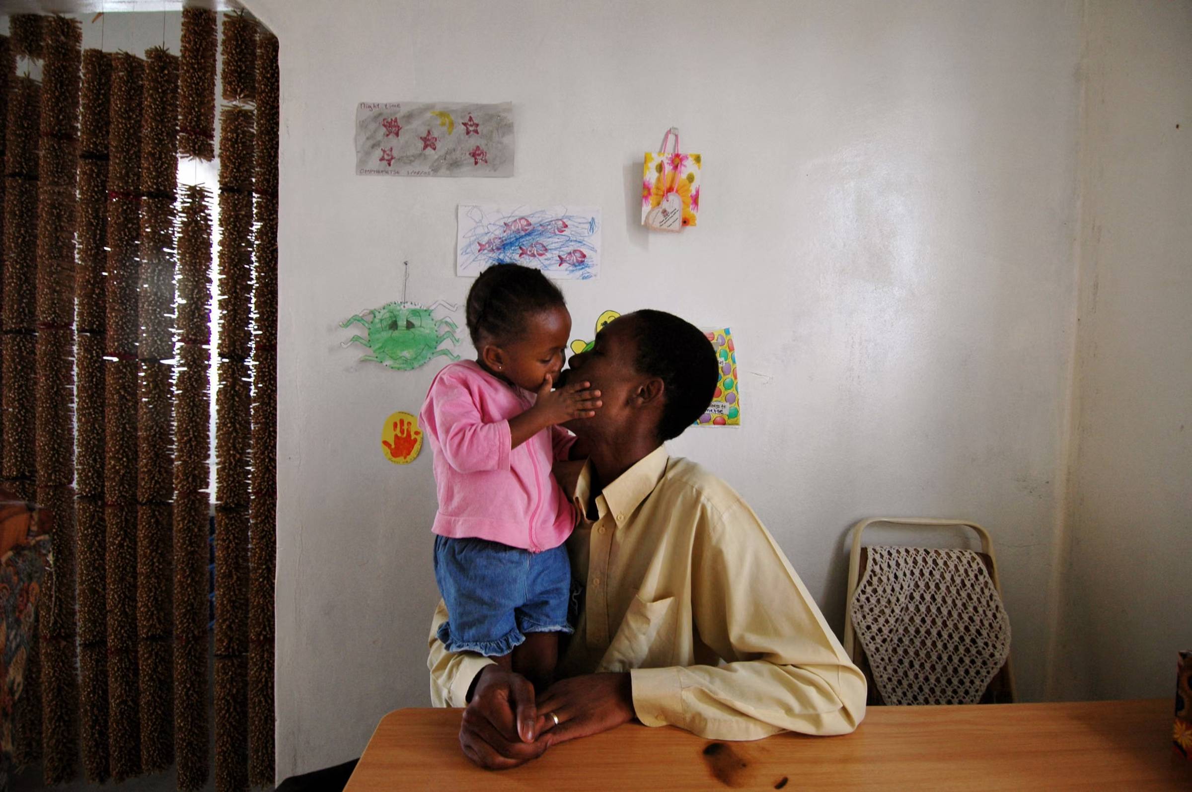 A girl in a pink sweater holding her mom's face and giving her a kiss