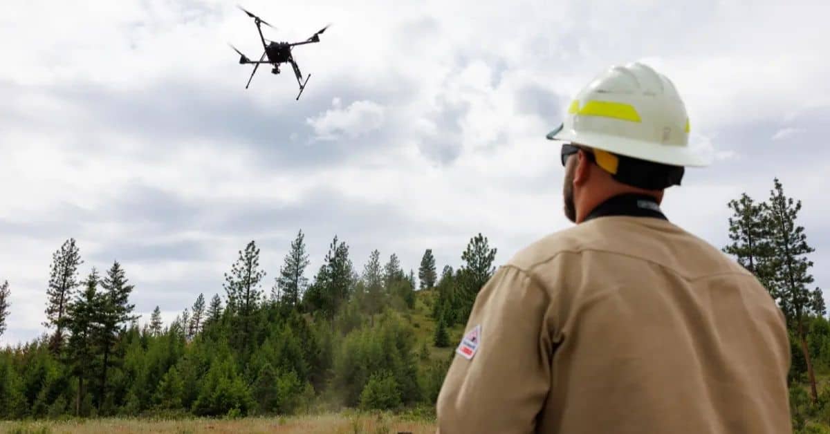 Person in a brown jacket and hard hat flying a drone above their head