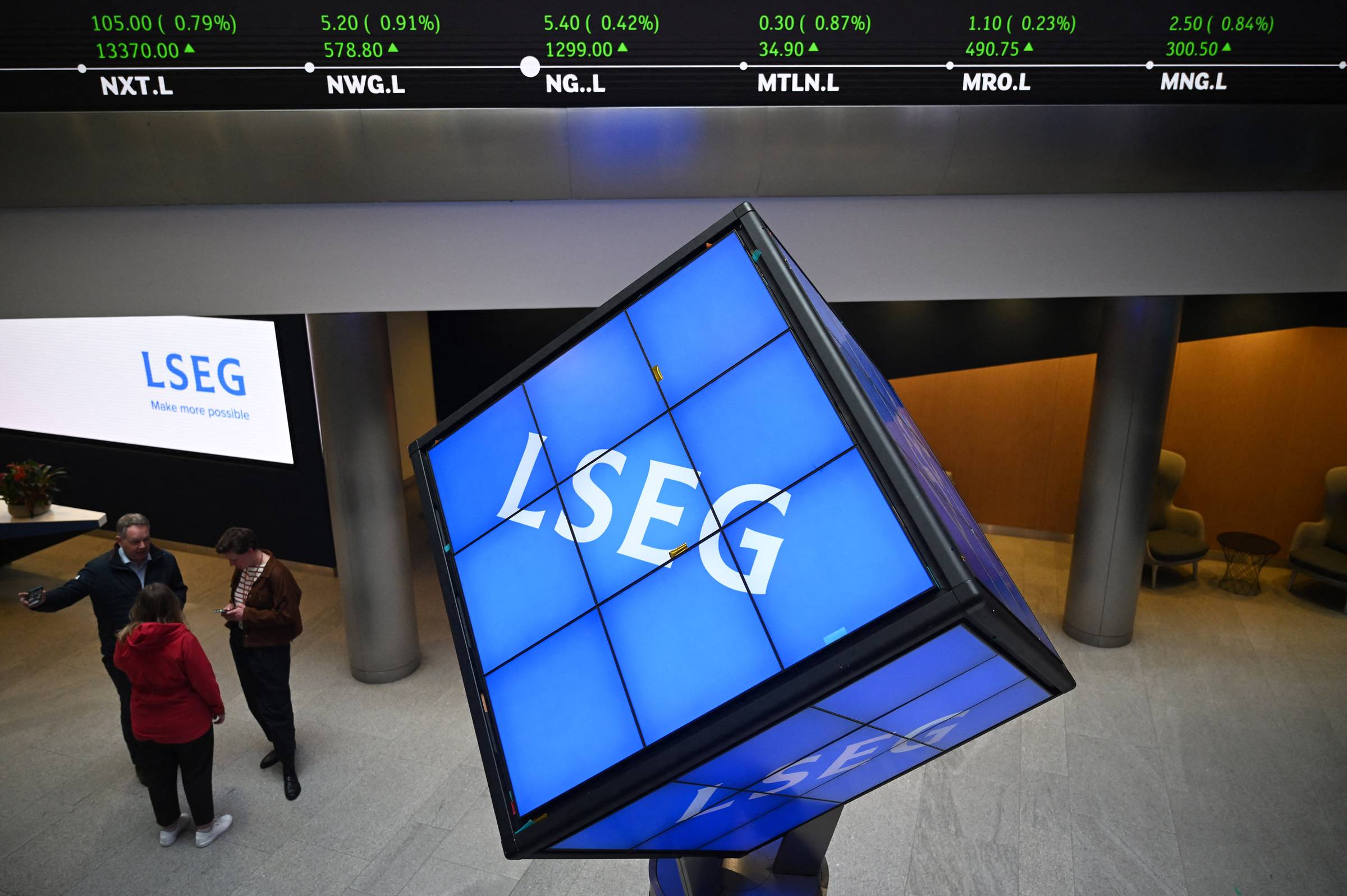 A large tilted video display screen showing the LSEG logo on a blue background in an indoor venue, with three people standing nearby and an LSEG signage visible in the background.