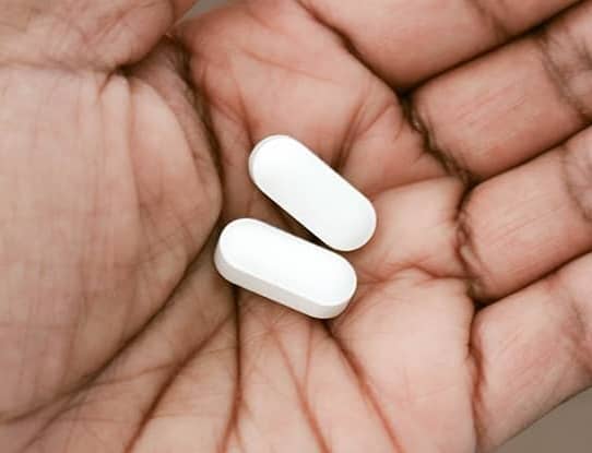 Two white pills in a person's hand