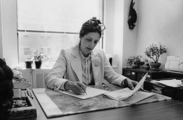 Black and white photo of a person sitting at a desk, writing on a piece of paper