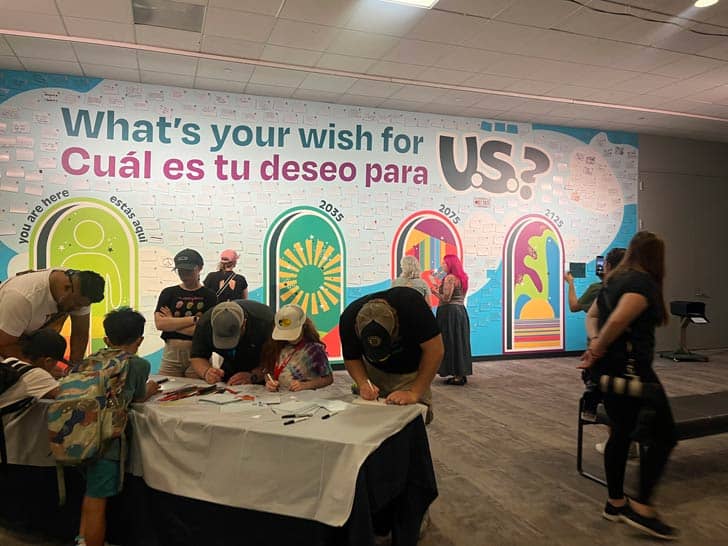 Wish wall behind people writing at a table