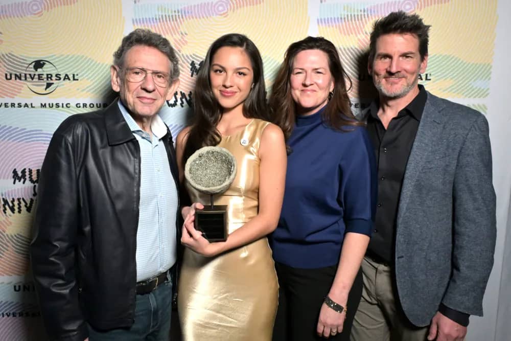 Olivia Rodrigo holding an award with three people standing next to her
