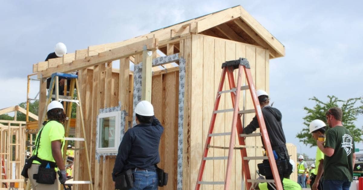 Young people in hard hats and tool belts building a tiny home