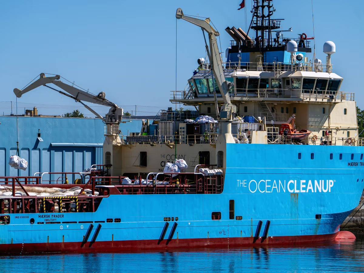 A massive blue ship with "The Ocean Cleanup" on the side in white letters