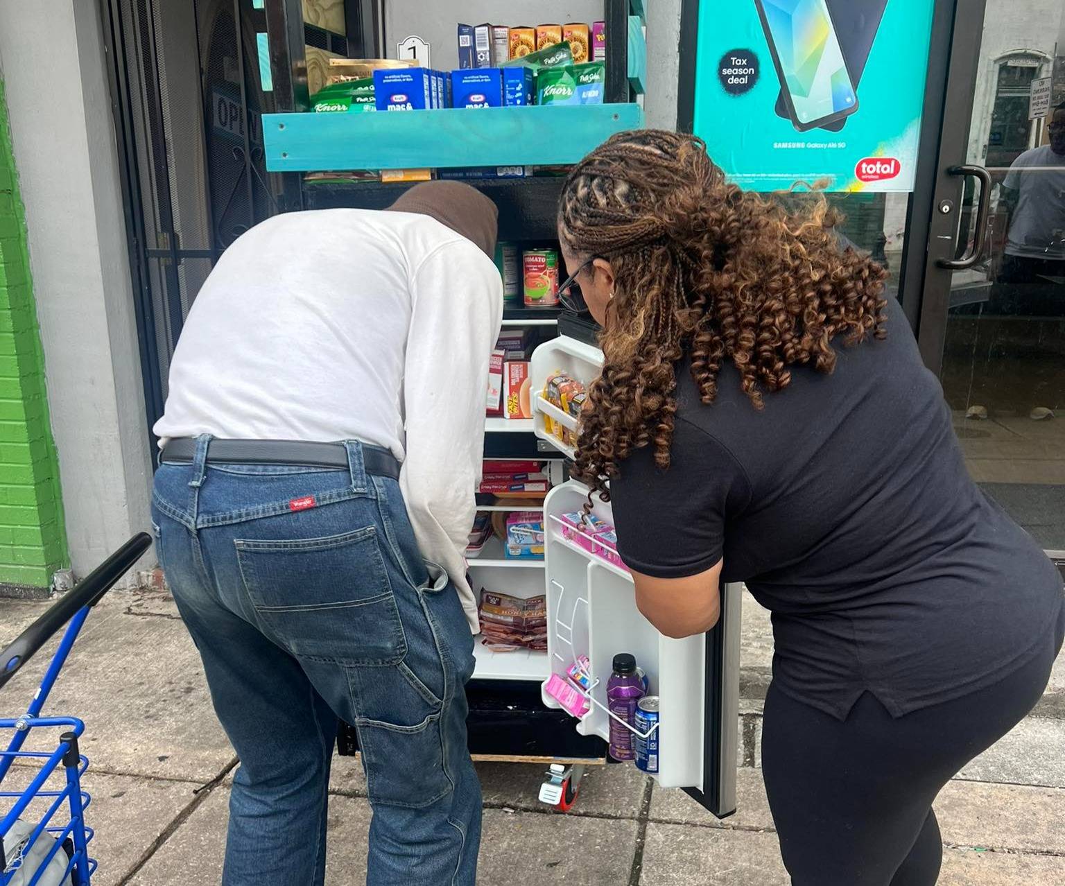 Two people looking inside a refrigerator outside a store