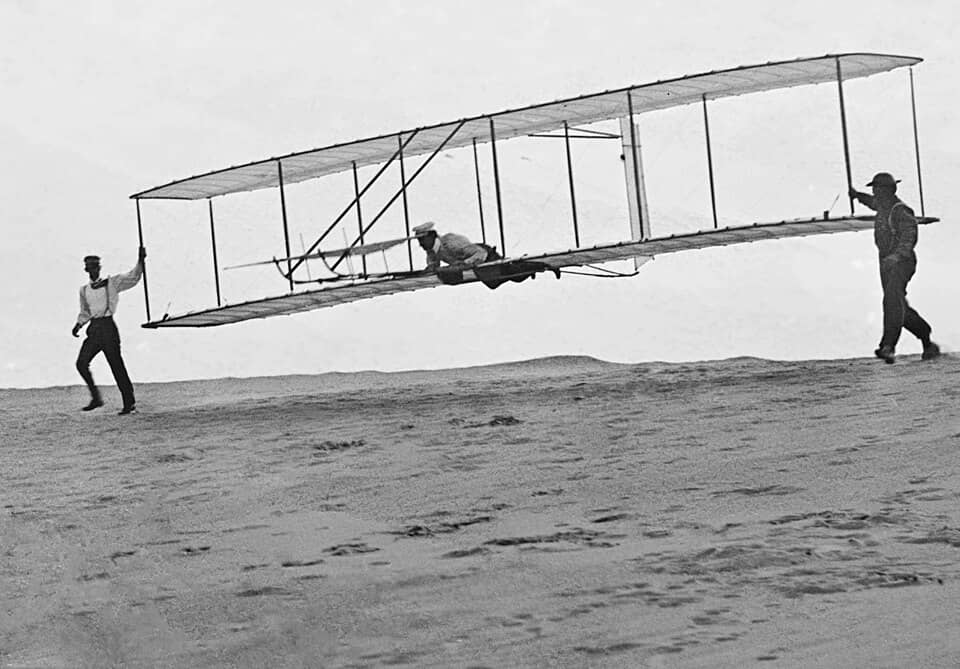 Black and white photo of three people helping a hand glider take off