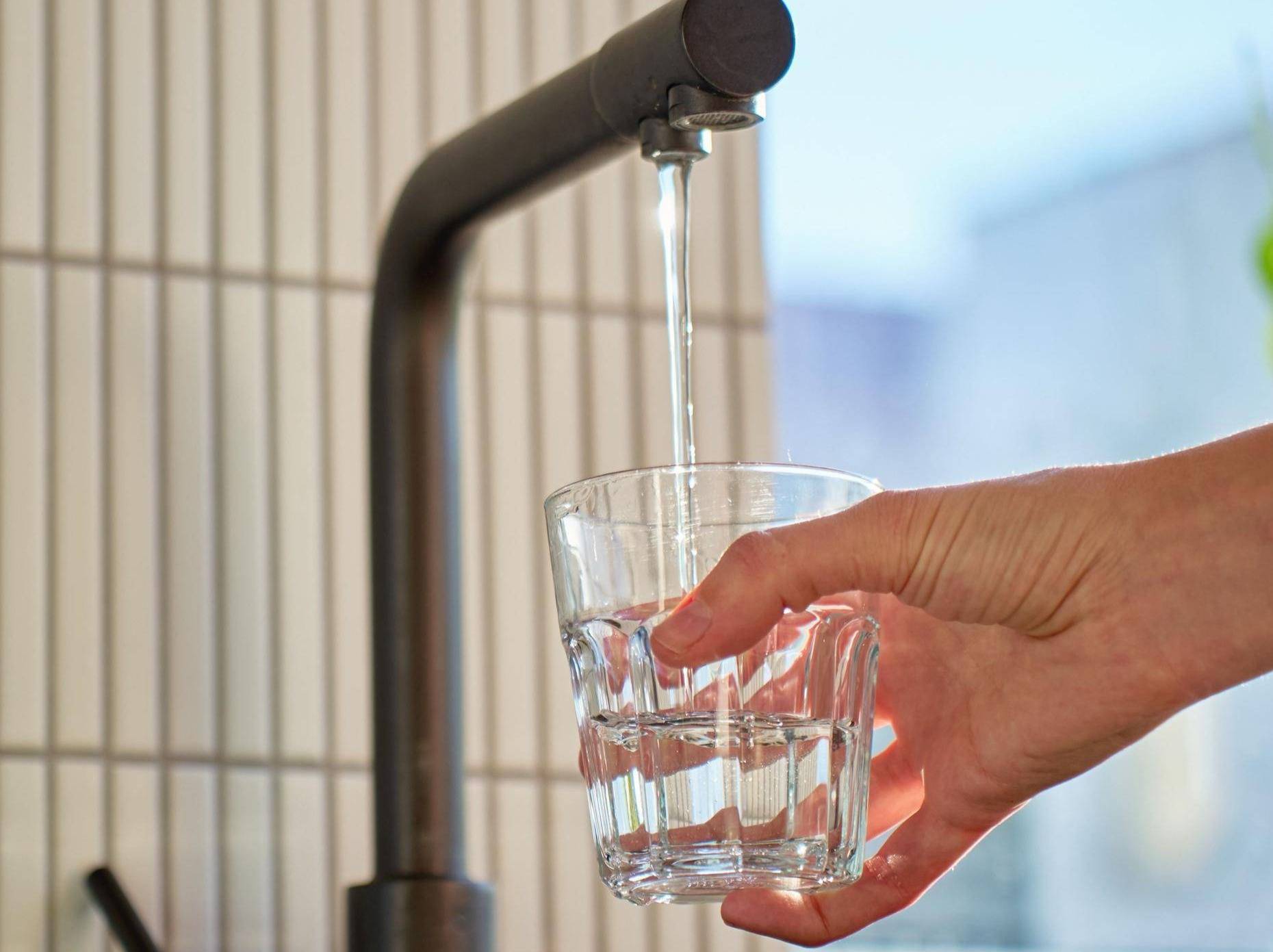 Person holding a clear glass under a water spigot