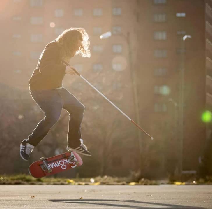 Person with a white cane doing a skateboard trick