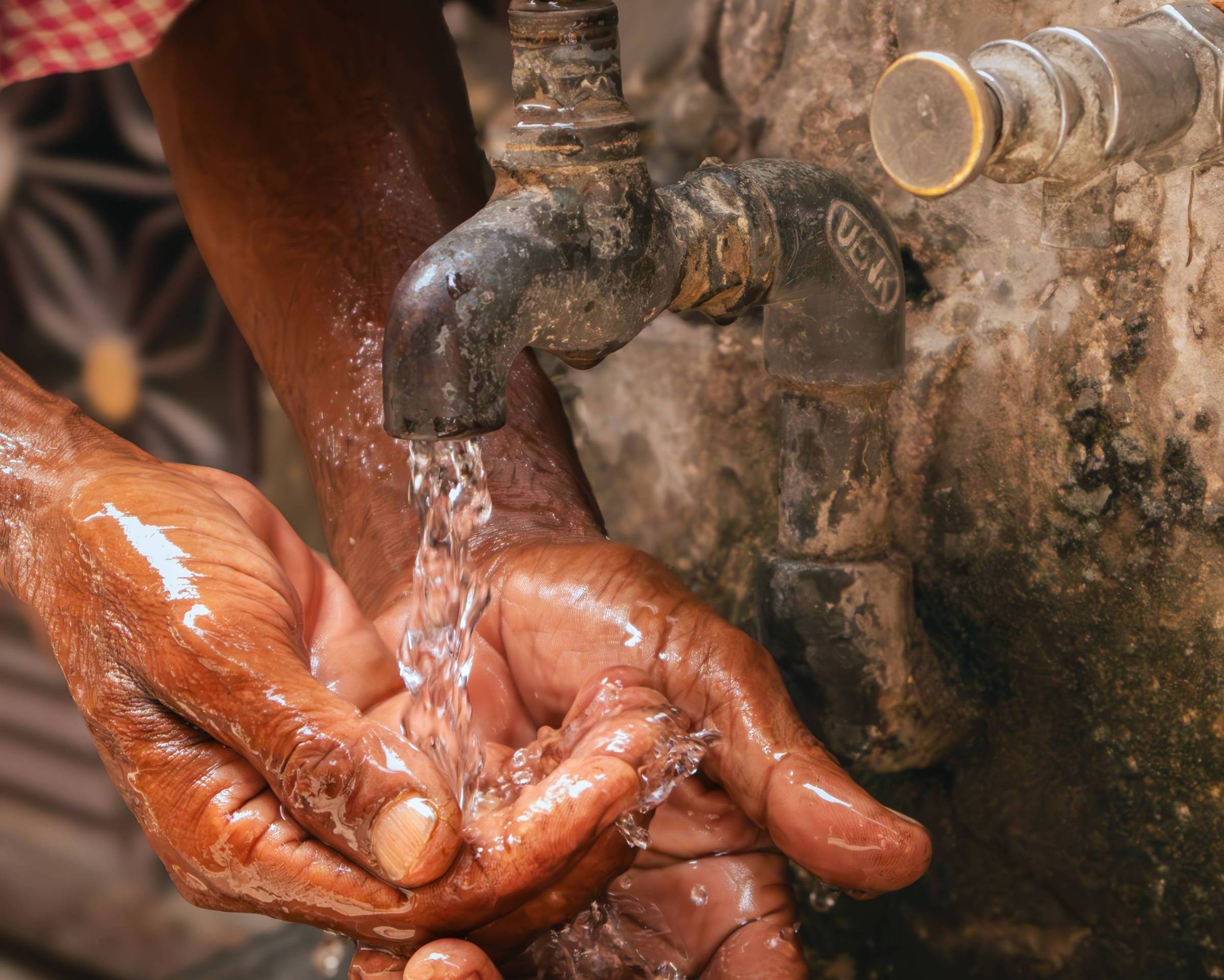 Hands covered in water coming out of a tap, the tap is affixed to a concrete wall 