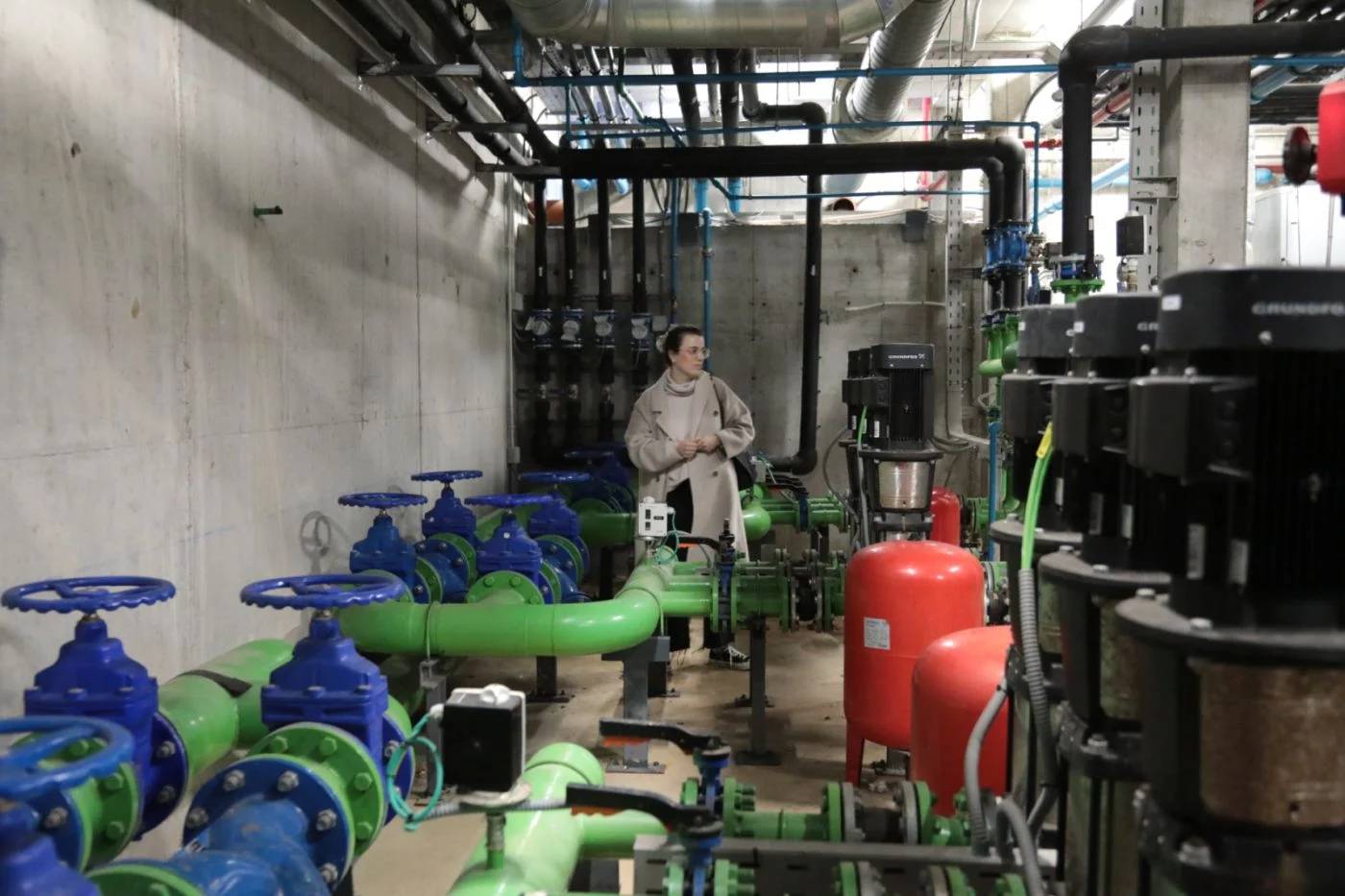 Person standing in a concrete room that's filled with blue, green pipes