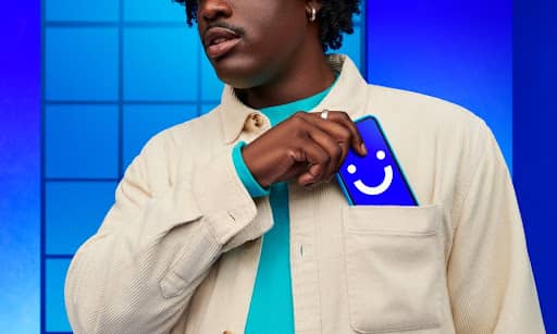 A person pictured from mid-face to chest pulling a smartphone with a blue screen and smiley face on it