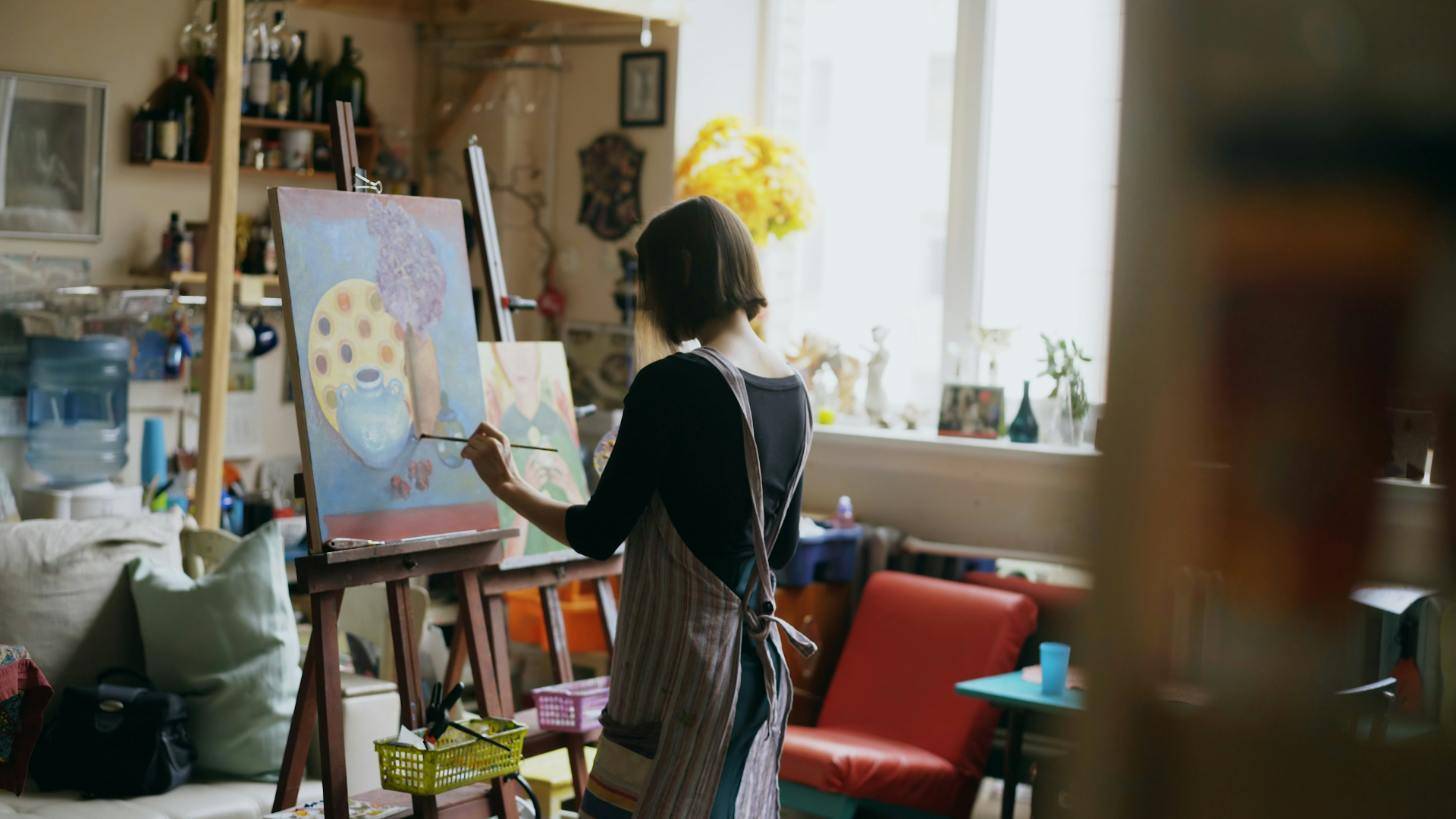 A person wearing an apron painting on a canvas in a living room-style room