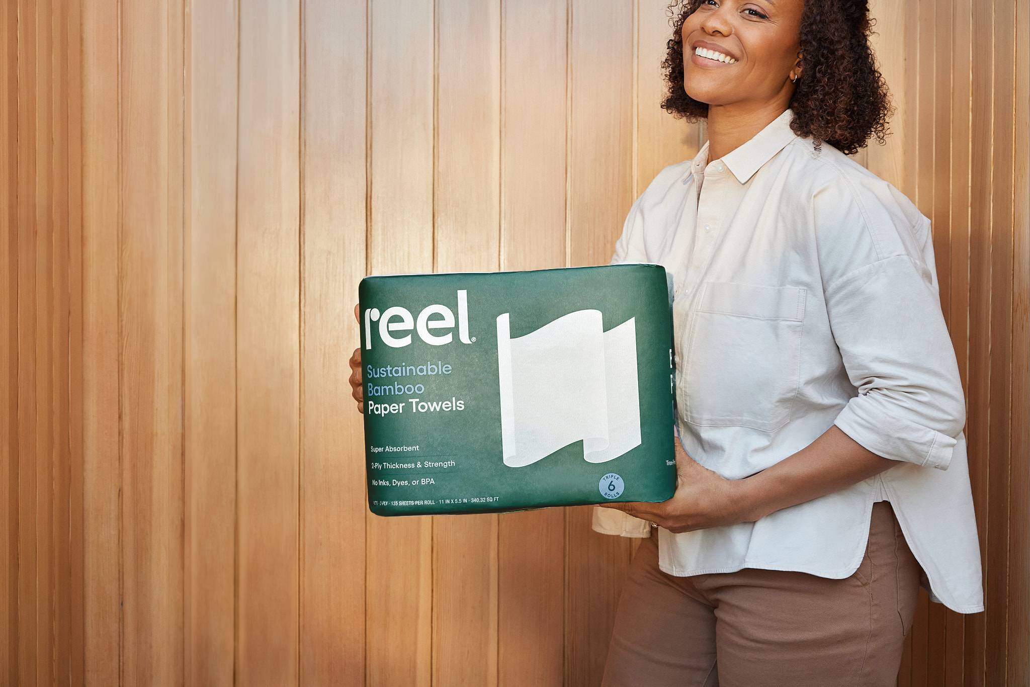 A person in a white button-down shirt holding a pack of Reel sustainable bamboo paper towels