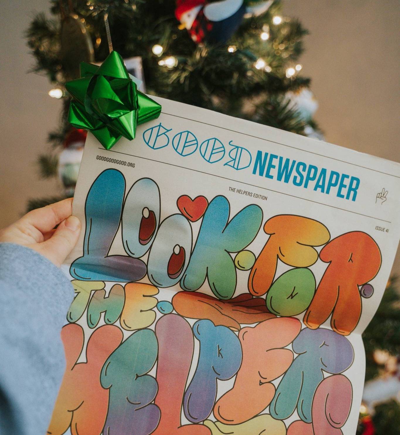 A print Goodnewspaper in front of a Christmas tree with a green bow on the corner