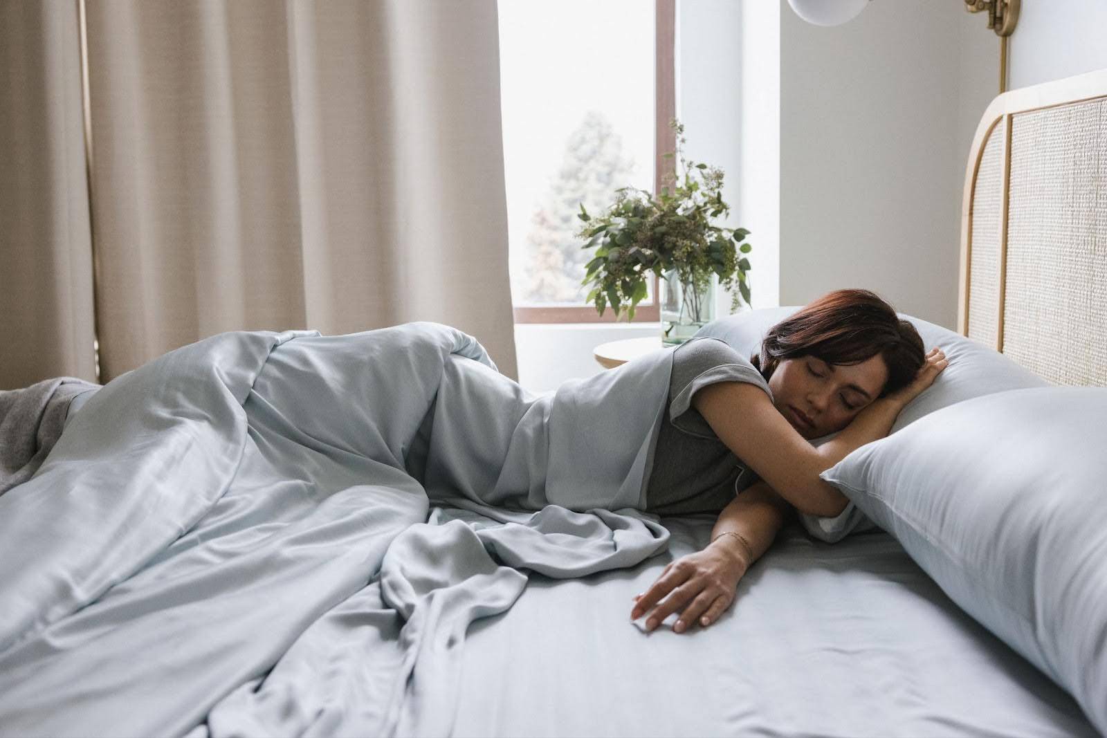 Person laying in a bed made with light grey colored sheets