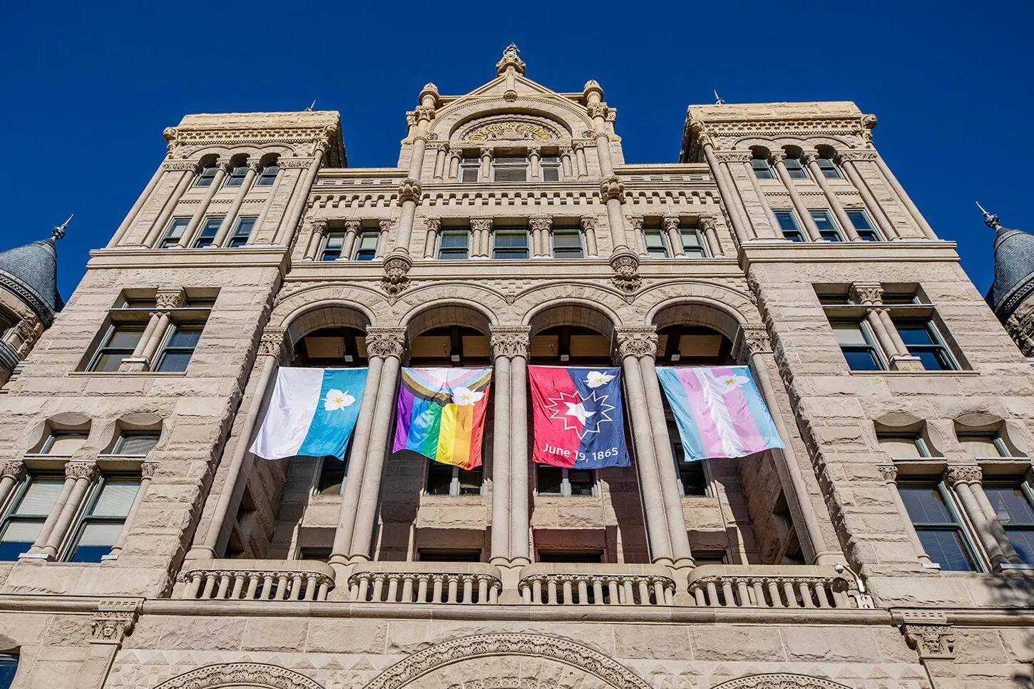 Utah state flag, progress Pride flag, Juneteenth flag, and trans flags hanging from capitol building