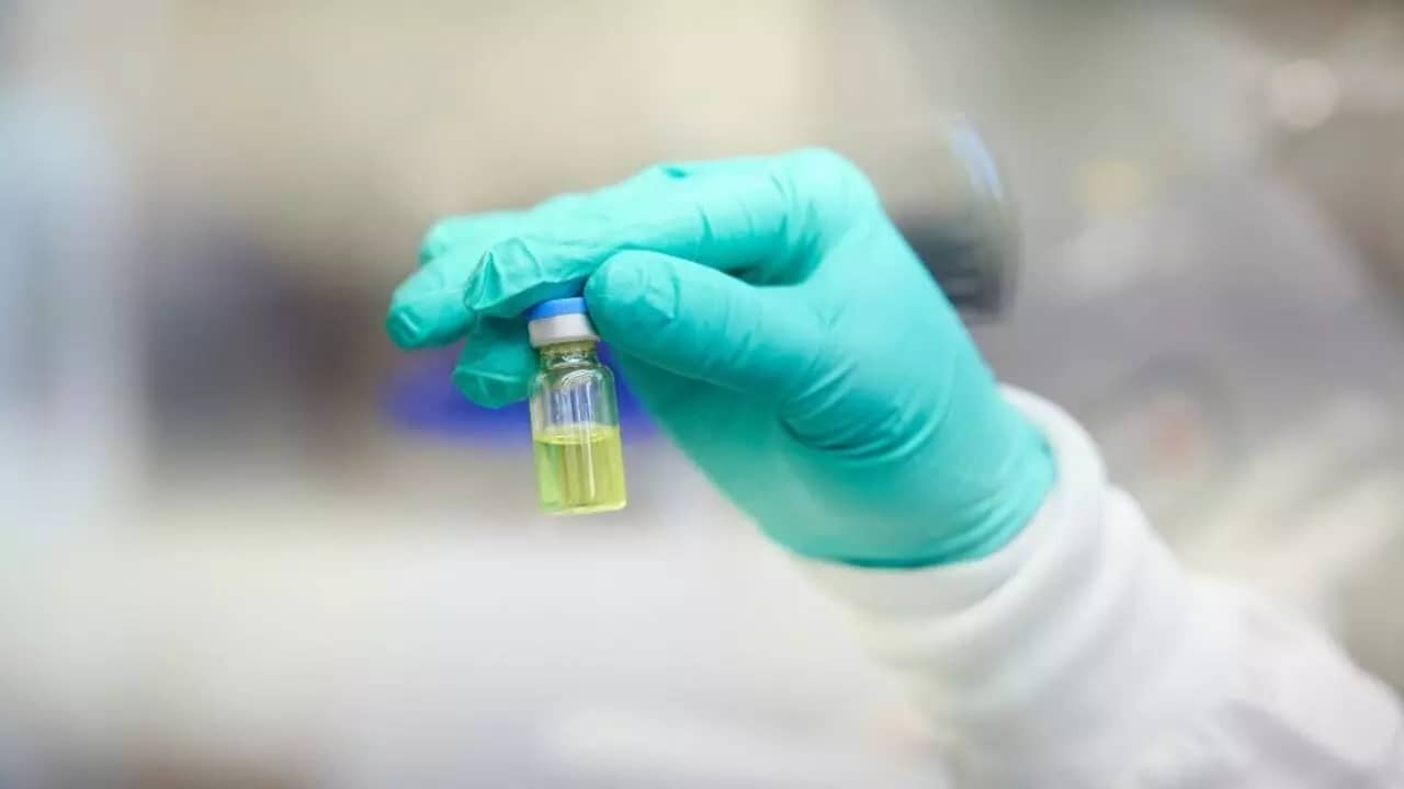 Hand wearing a teal latex glove holding a vial of lenacapavir