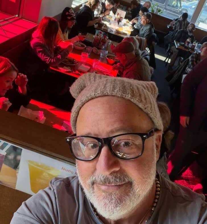 Selfie of a man in a beanie and glasses with tables at a restaurant full behind him