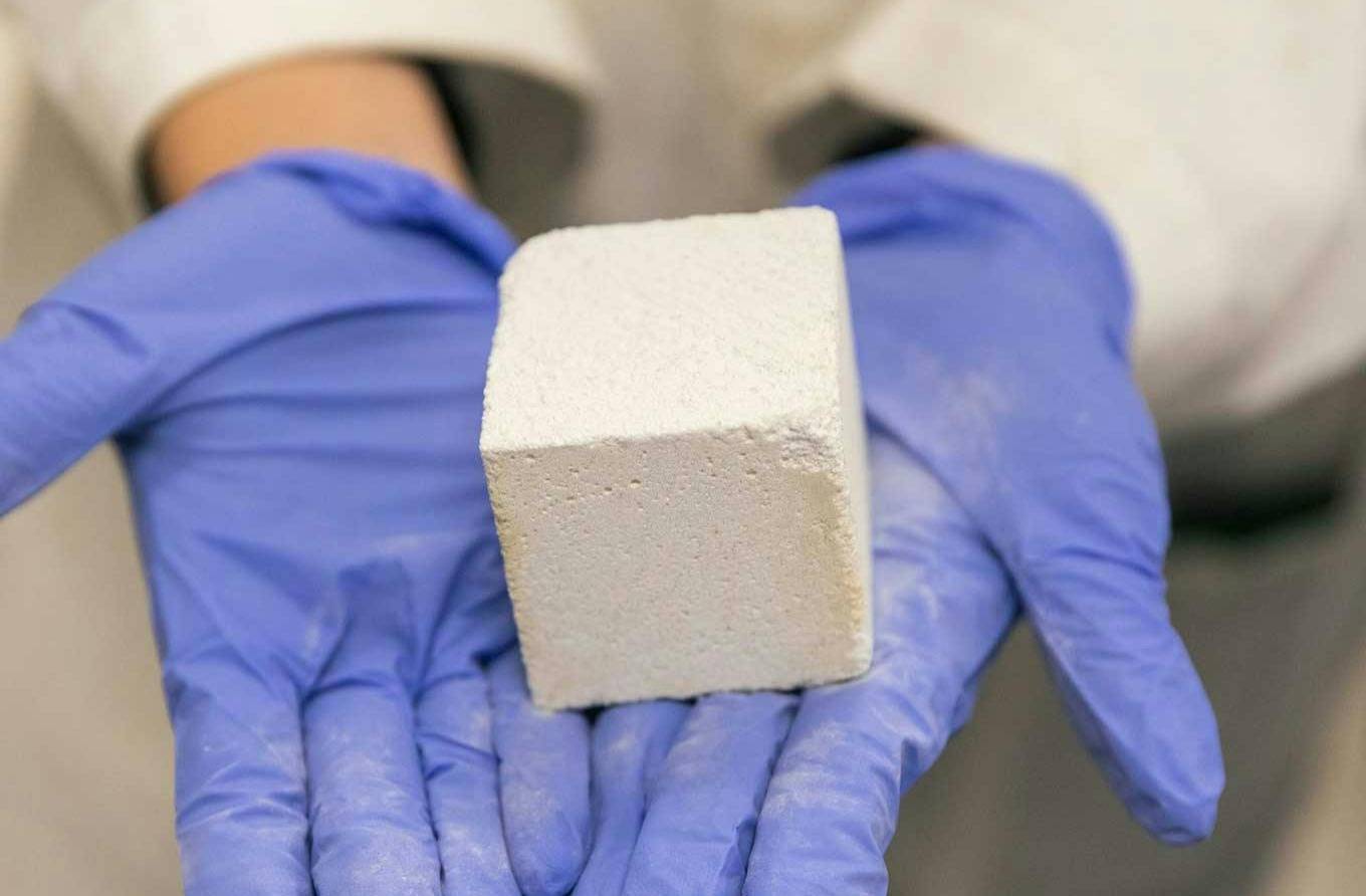 A pair of hands wearing blue latex gloves holding a small block of light grey-colored concrete
