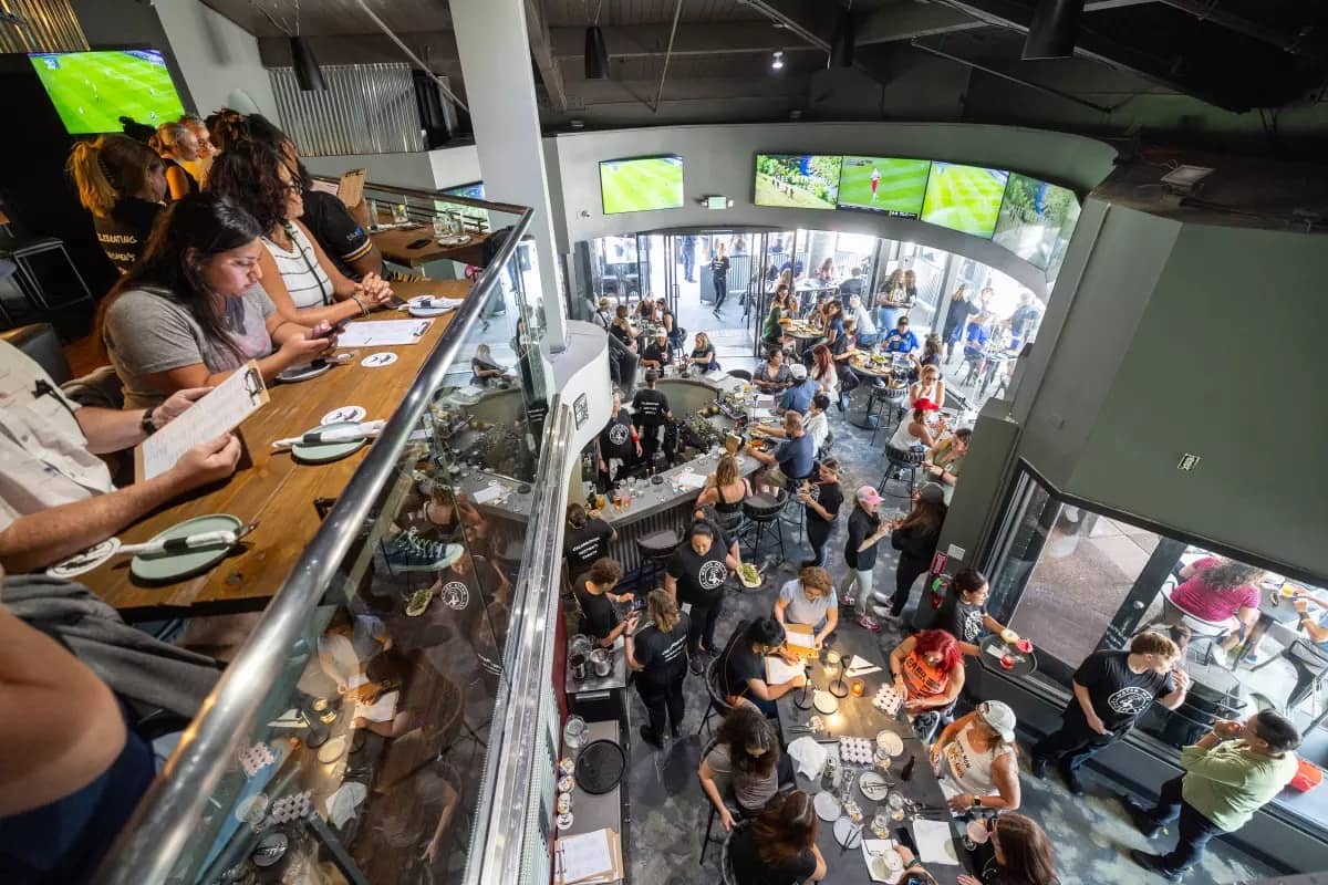 Overhead photo of a packed bar with TV screens on the walls and people sitting around tables with food and drinks