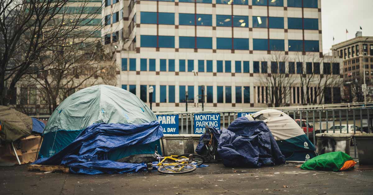 Two tents, a bicycle, tarps on a concrete ground with buildings in the background