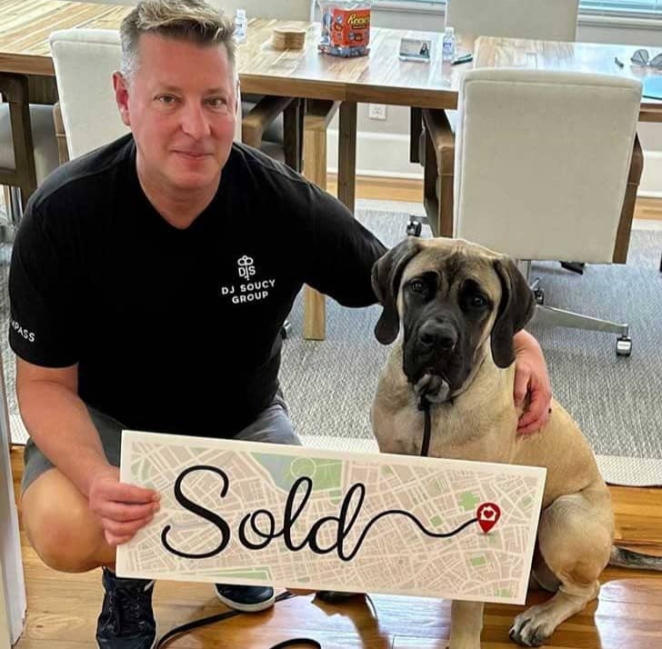 Person in black t-shirt next to a dog holding a "Sold" sign