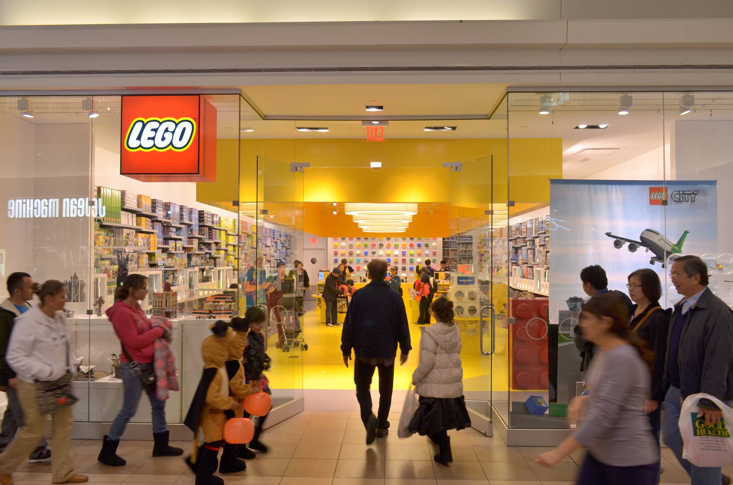 The entrance of a LEGO store with glass walls and doors and people walking in and past it