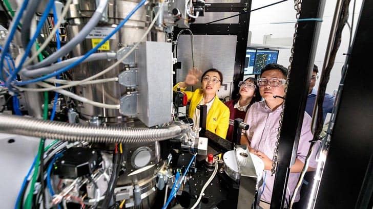 Four students wearing protective eyewear looking at a piece of complex machinery