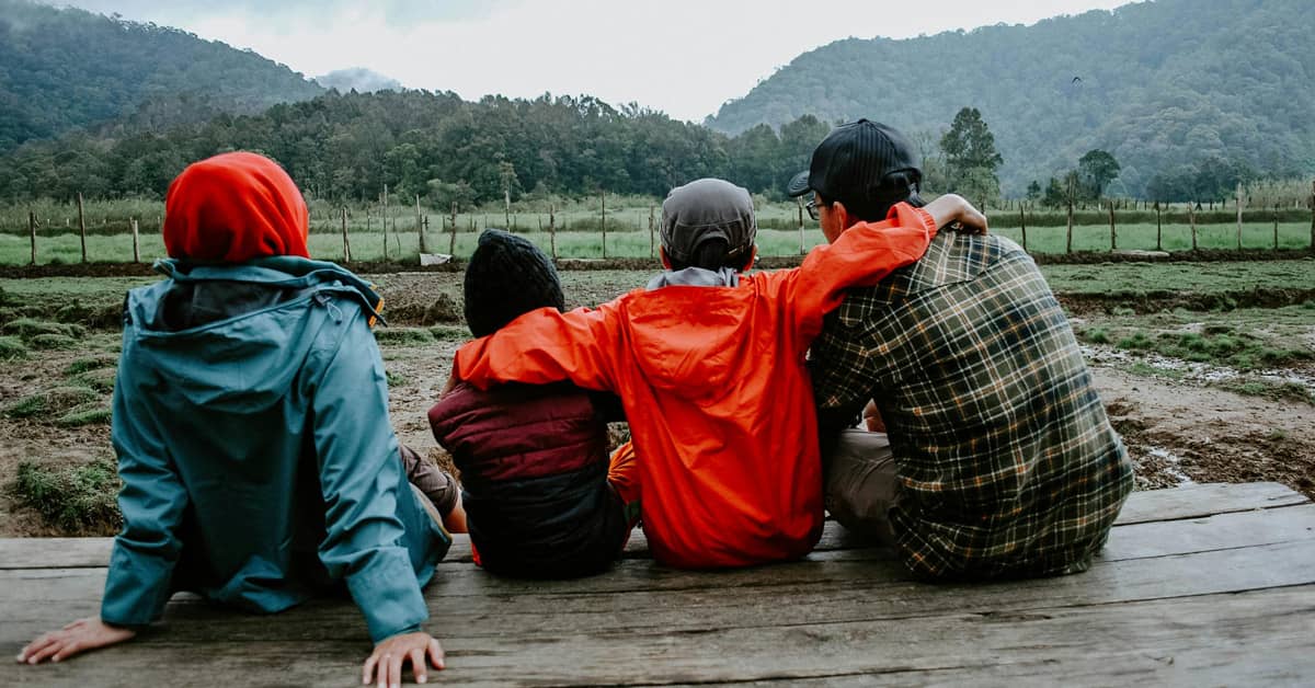 Four people sitting on a wooden platform looking out at a field