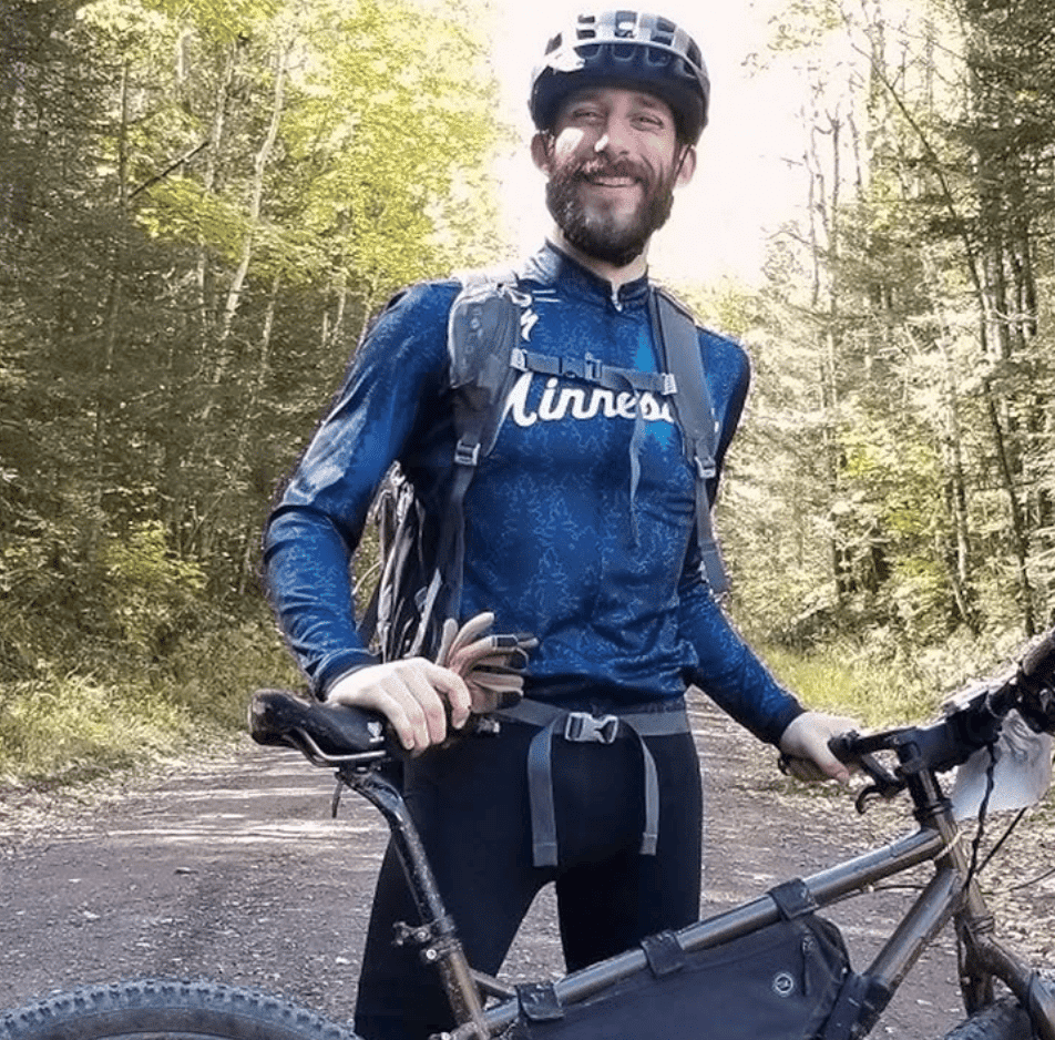 Alex Pretti standing next to his bike, wearing a helmet, smiling at the camera