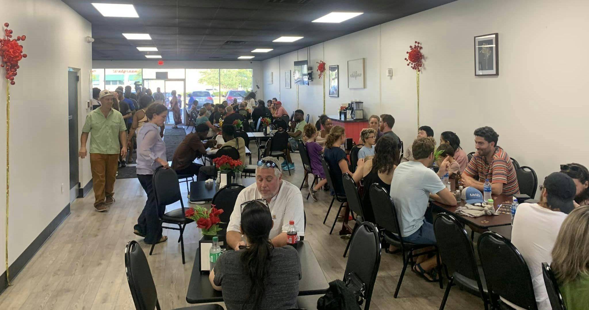 A Haitian restaurant with long tables filled with people and a line out the door in the background 