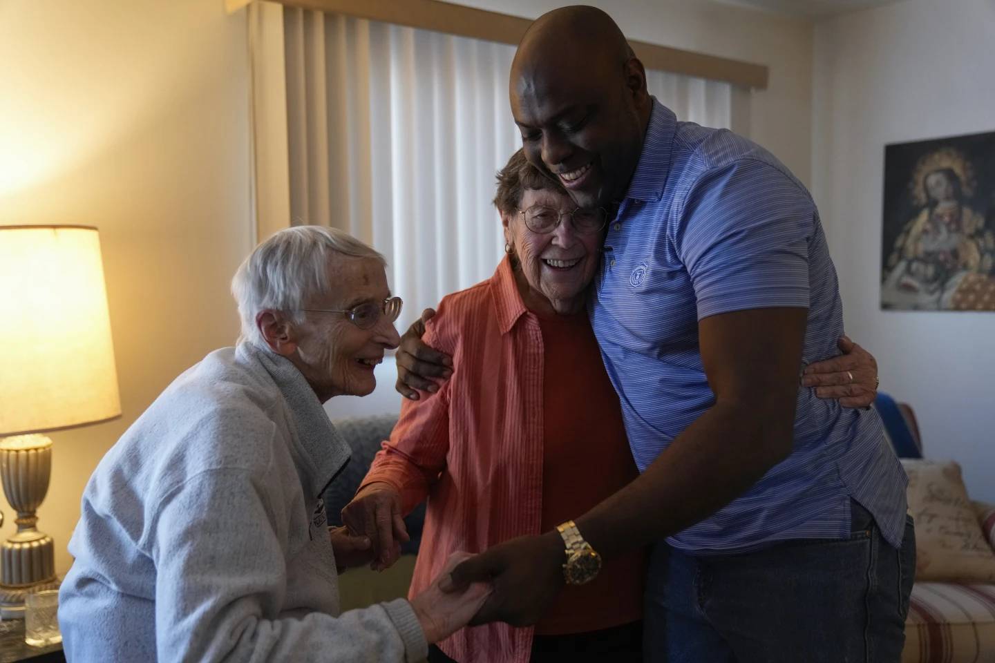 A Black man in a blue polo hugging two older white women