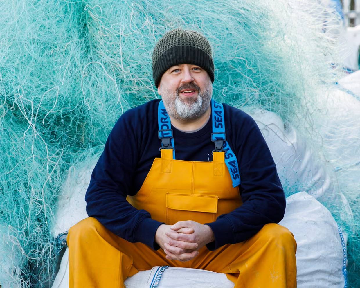 Ian Falconer sitting on a bag filled with plastic nets, with more piled behind him