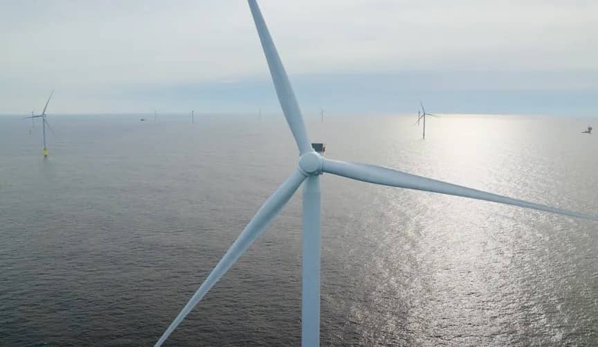A close-up photo of the blades on an offshore wind turbine with more turbines visible in the water in the distance