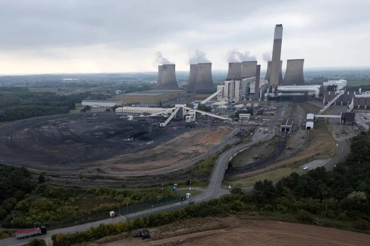 A wide, overhead photo of the power station with several concrete towers, coal-colored ground in the foreground, and other industrial parts of the power plant