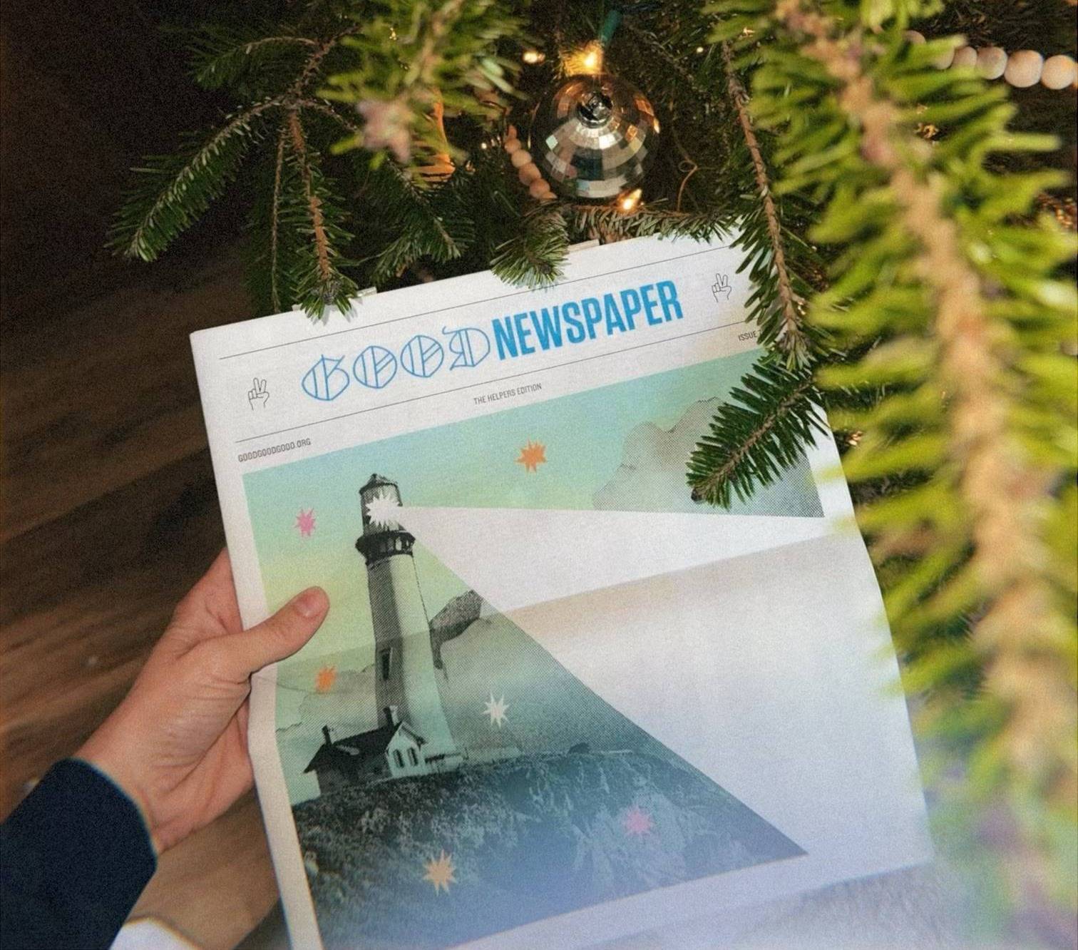 Hand holding a Goodnewspaper next to a Christmas tree