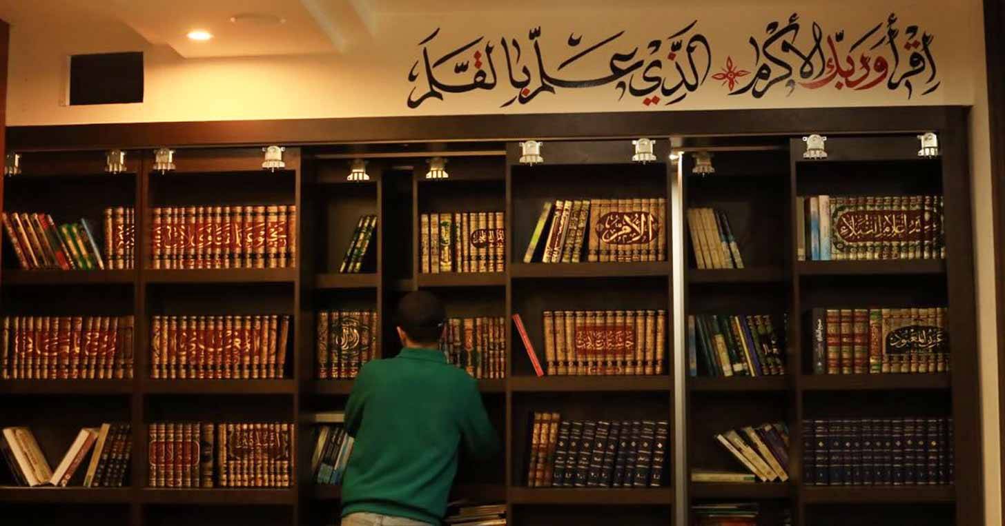 A person in a green sweater in front of a wall filled with books