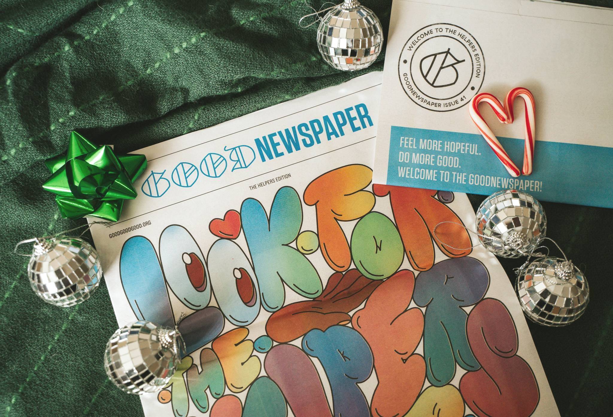 Print newspaper titled "Goodnewspaper" on a green cloth with mirror ball ornaments, a green bow, and candy canes