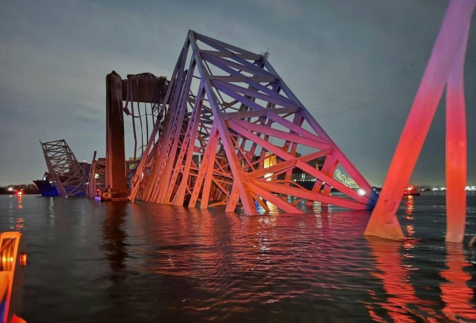 Pieces of the collapsed bridge in water lit up by blue and red emergency lights